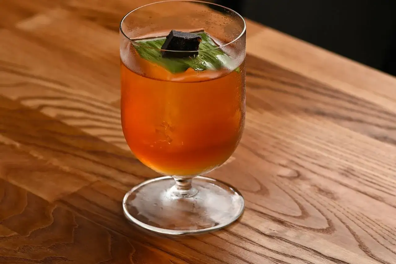 Orzeźwiający koktajl Mai Tai w szklance z lodem, ozdobiony liściem i kostką ciemnego cukru.