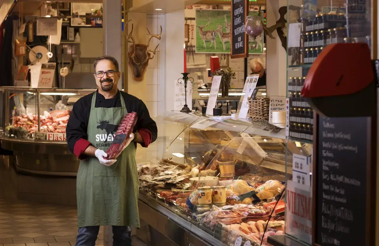 Butiksanställd i stora saluhallen håller stolt upp ett stort stycke kött.