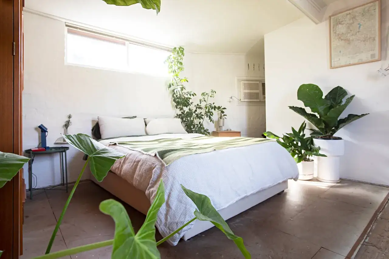 Dormitorios matrimonio sin cabecero, con cama baja, muchas plantas y luz natural. Un espacio acogedor y fresco.