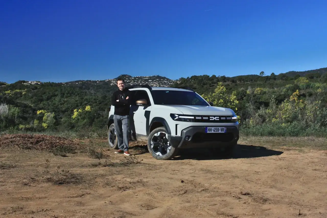 Mężczyzna stoi obok białej Dacia 4x4 na tle wzgórz.