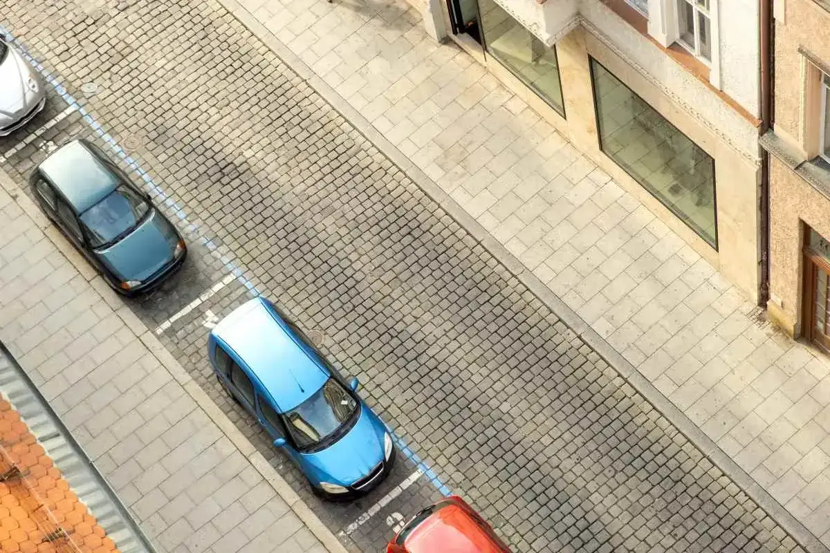 Widok z góry na ulicę z zaparkowanymi samochodami. Widać kilka miejsc parkingowych, co pozwala ocenić, ile miejsc parkingowych na mieszkanie jest dostępnych w tej okolicy.