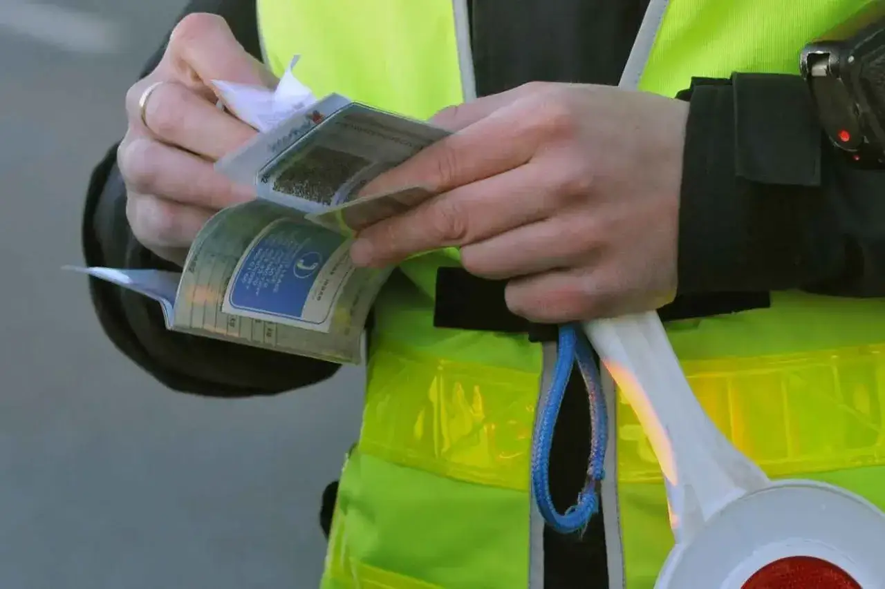 Policjant w kamizelce odblaskowej przegląda dokumenty. Może to oznaczać mandat za brak przeglądu technicznego pojazdu.