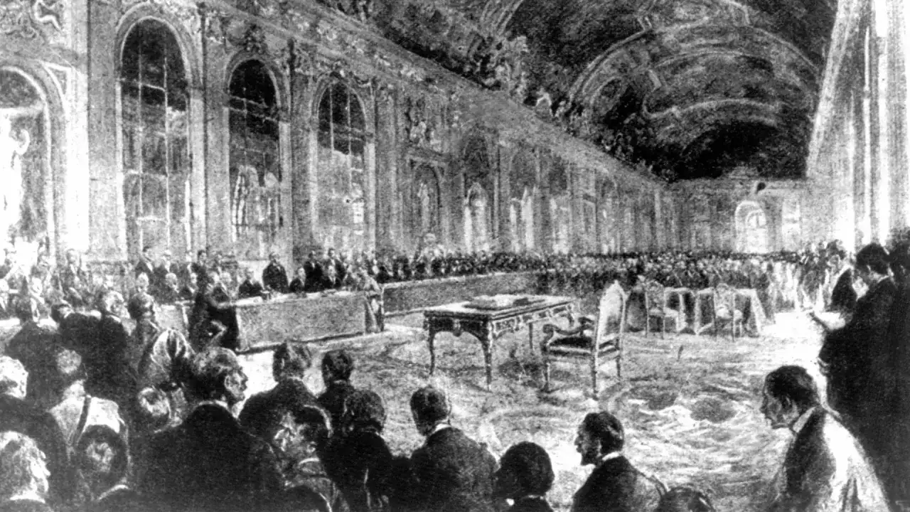 Großer Saal mit vielen Menschen, die sich versammelt haben. Ein Tisch mit Stuhl steht im Vordergrund. Dies ist eine Darstellung des Friedensvertrags von Versailles.