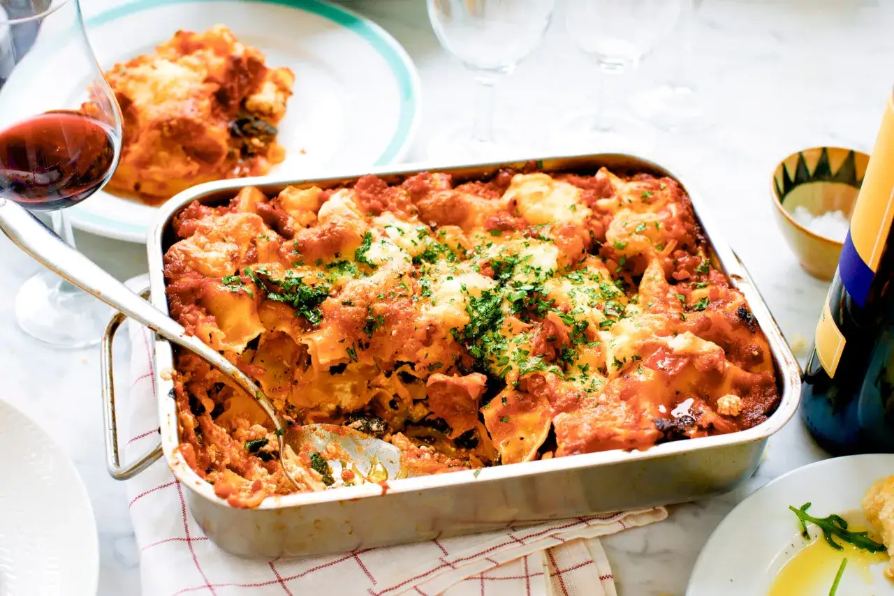 En nybakad vegetarisk lasagne i formen, toppad med ost och persilja. En sked är redo att servera.
