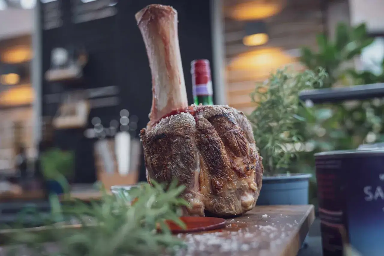 Ein saftiges Stück pulled beef mit Knochen, garniert mit Rosmarin, liegt auf einem Holzbrett.
