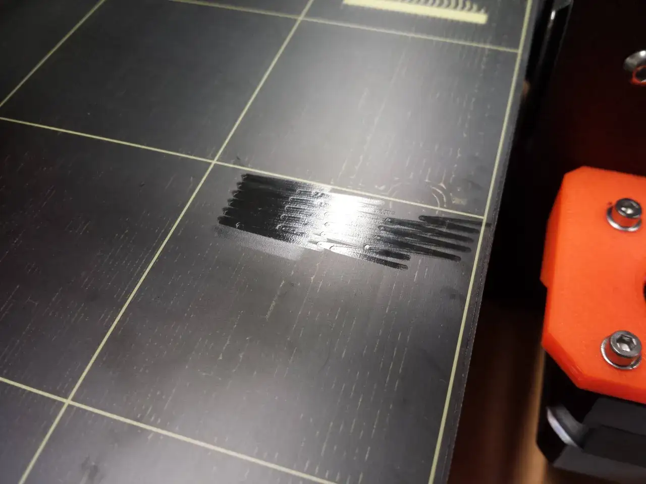 Linie filamentu na czarnej powierzchni stołu roboczego drukarki 3D, świadczące o udanej kalibracji drukarki 3d.