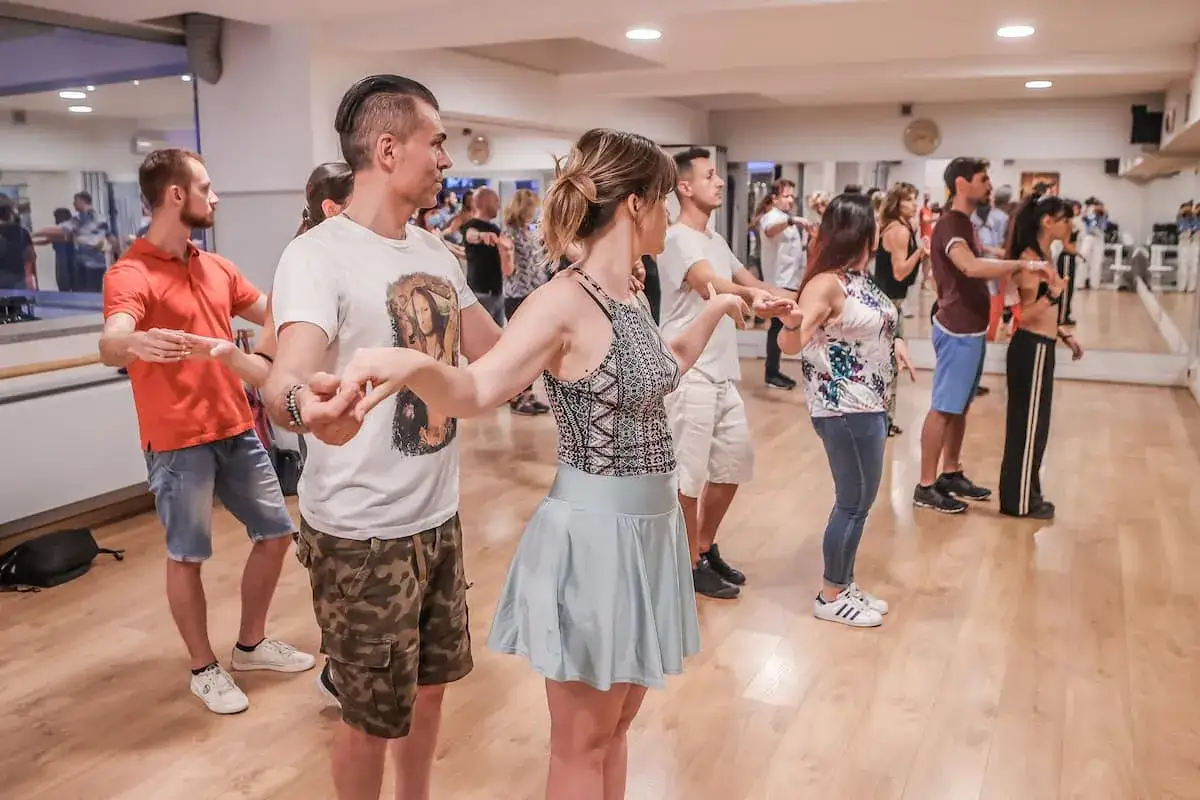Un gruppo di persone impara a ballare latino americano in una sala con specchi.