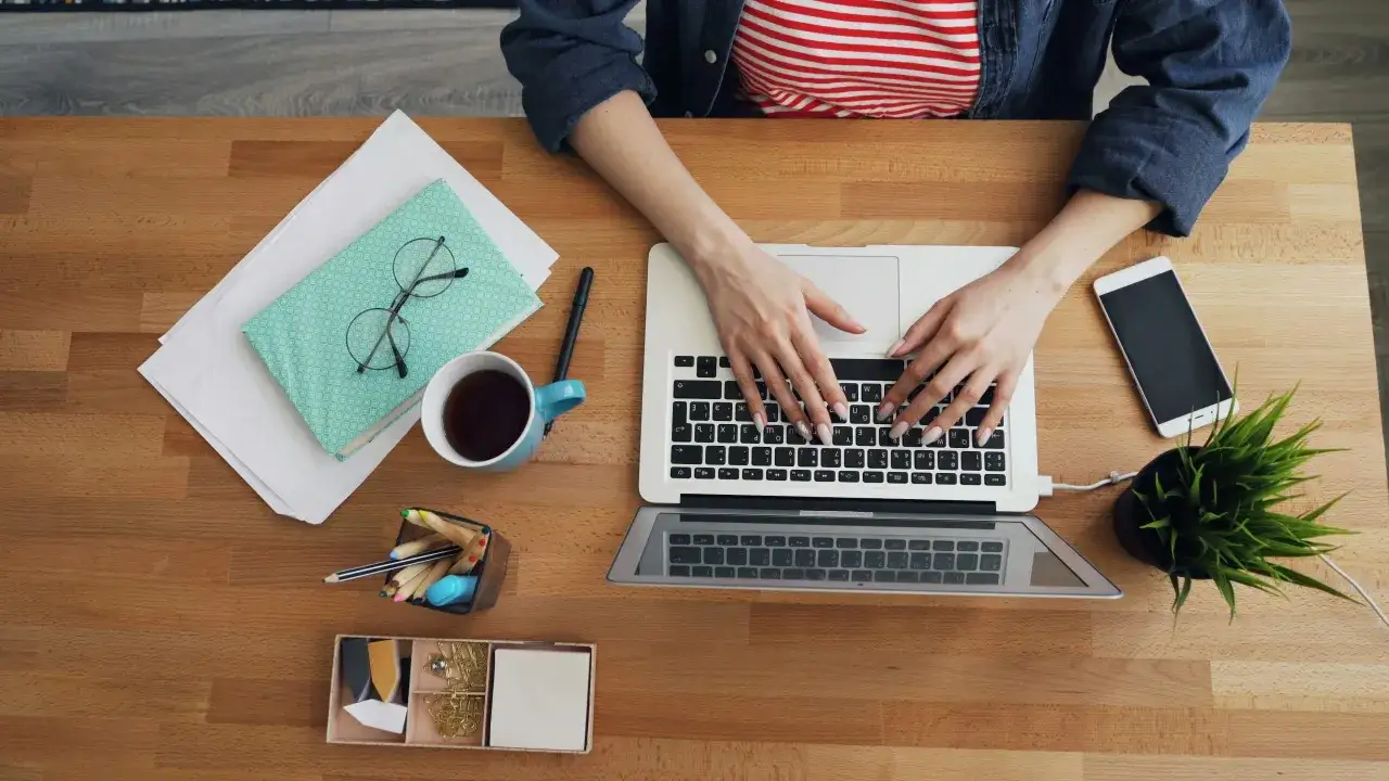 Kobieta pracuje na laptopie, obok kubek kawy, telefon i notatnik. To pokazuje, co można robić po marketingu: rozwijać swoje projekty.