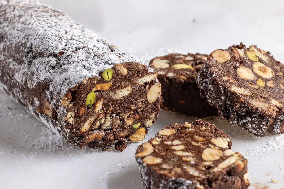 Salame di cioccolato senza uova ricetta della nonna, con biscotti, nocciole e pistacchi, spolverato di zucchero a velo.