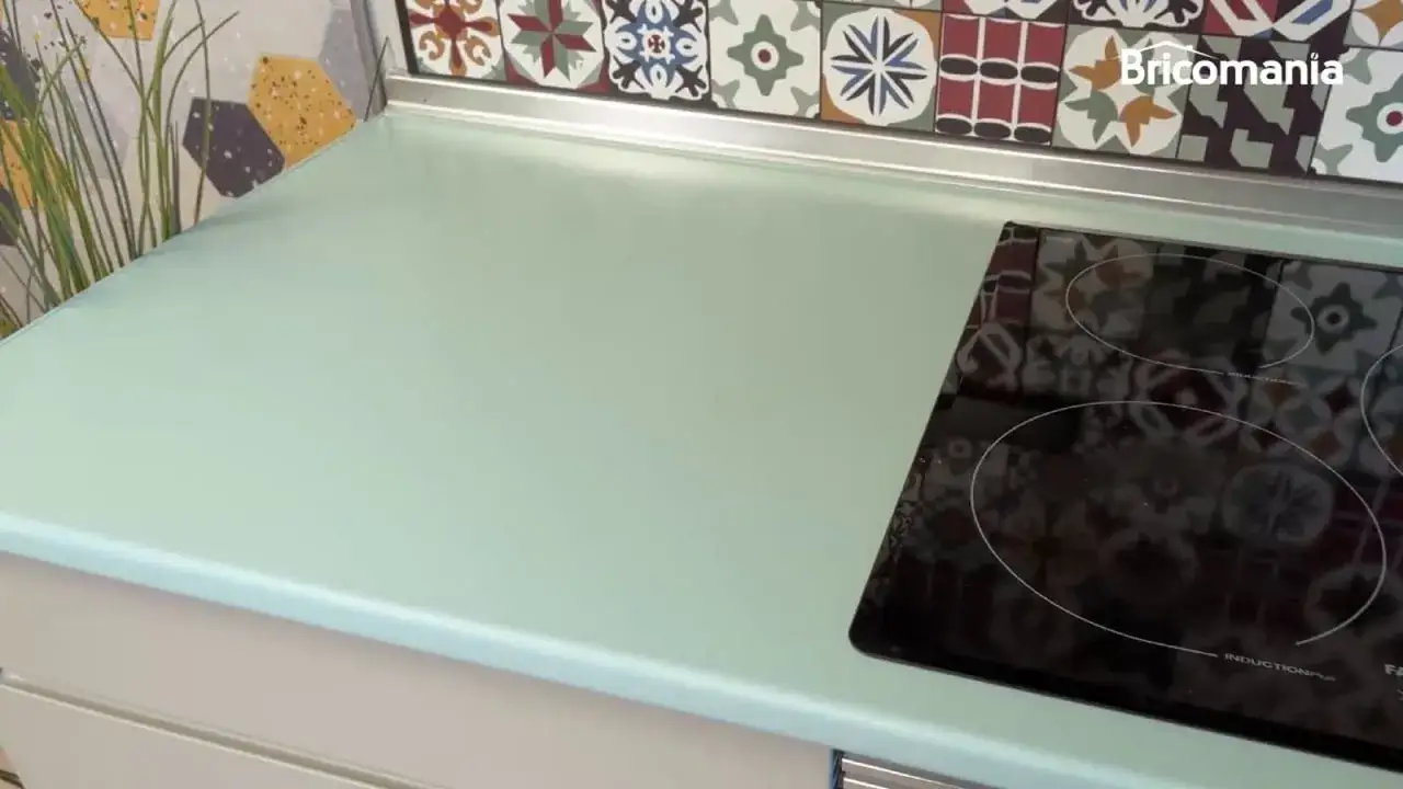 Encimera de cocina verde menta, con azulejos coloridos de estilo hidráulico detrás. Una placa de inducción negra está a la derecha.