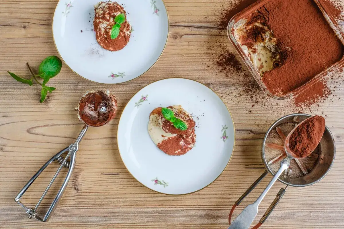 Tiramisu anrichten: Ein L&ouml;ffel voller K&ouml;stlichkeit, bereit zum Servieren auf zarten Tellern, best&auml;ubt mit Kakao.
