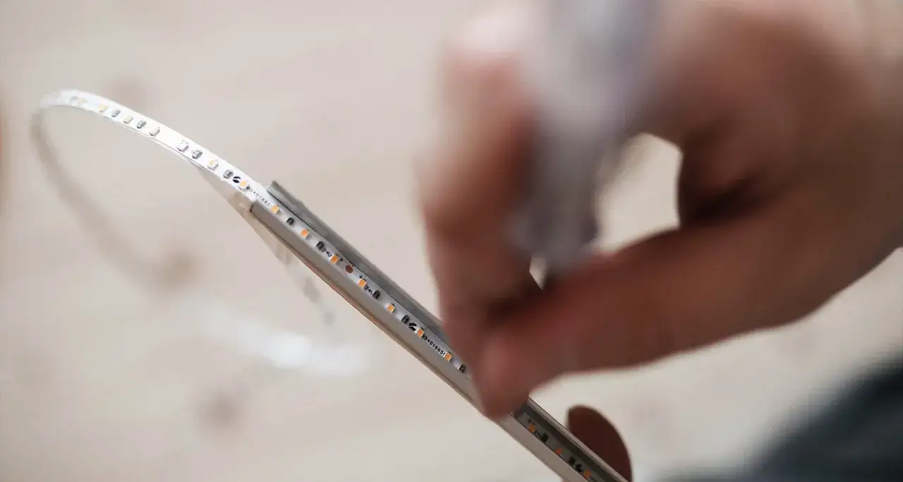 Montaż taśmy LED w aluminiowej listwie. Dłoń precyzyjnie układa diody.