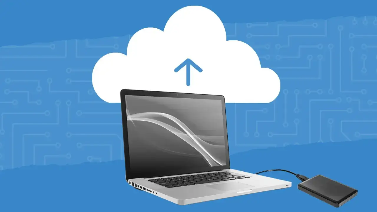 Laptop z podłączonym dyskiem zewnętrznym pod chmurą z ikoną uploadu. Dowiedz się, jak sformatować dysk z systemem.