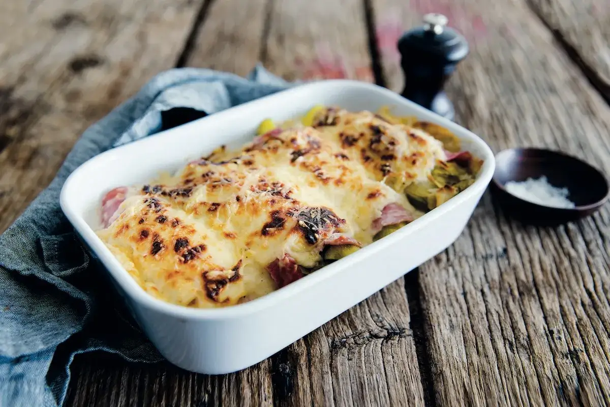 Un plat gratin&eacute; d'endives au jambon, recouvert de fromage dor&eacute;, sur une table en bois rustique.