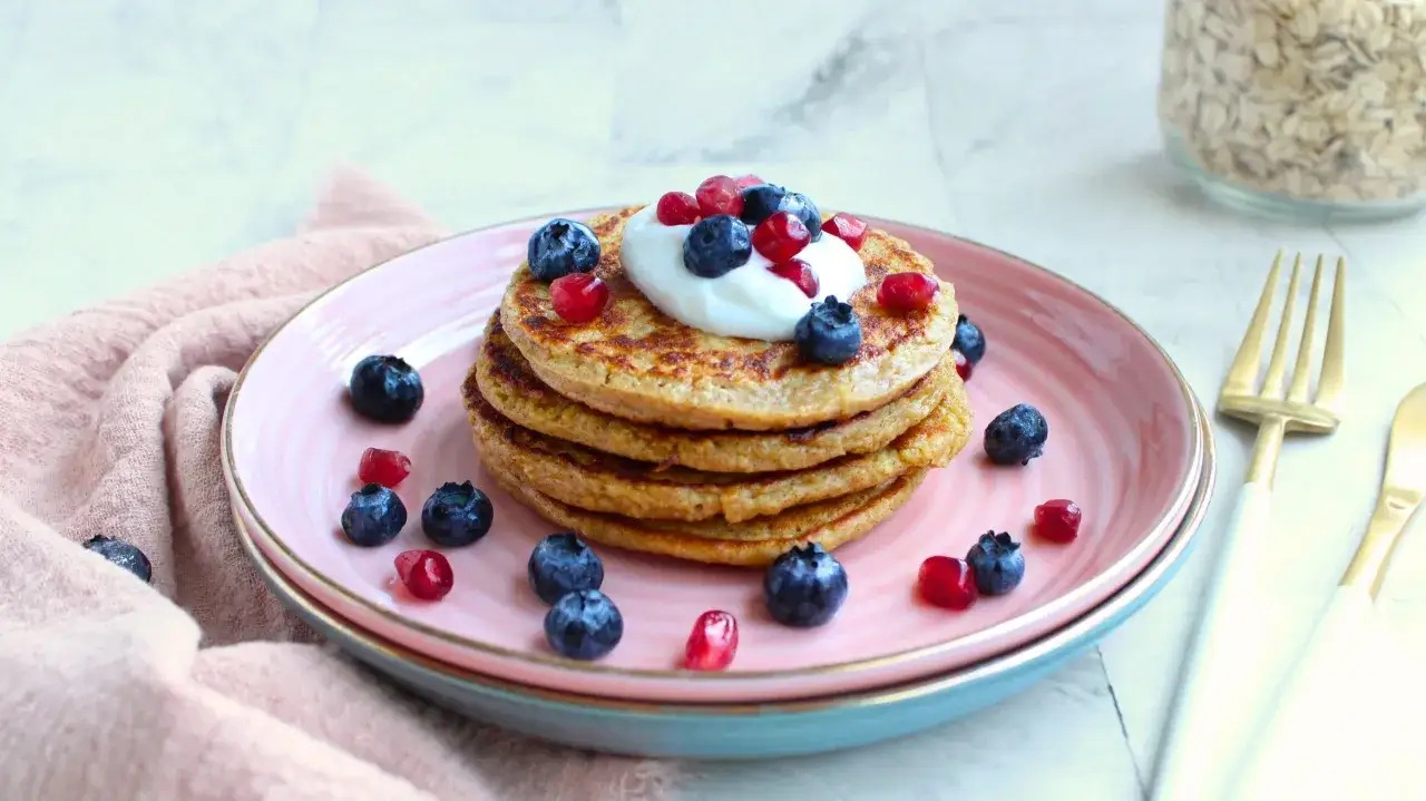 Deliciosas tortitas de avena apiladas, cubiertas con yogur, ar&aacute;ndanos y granada. Un desayuno saludable y colorido.