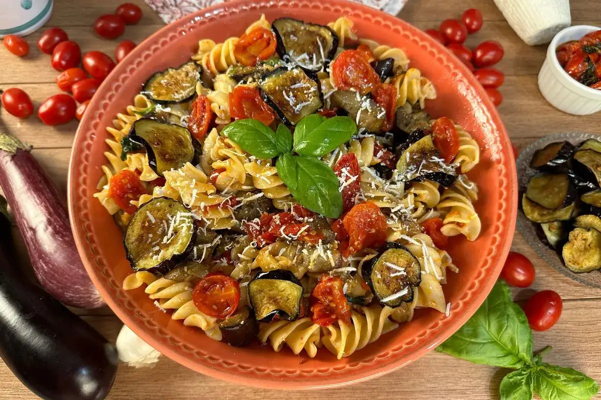 Pasta fredda alla norma con melanzane fritte, pomodorini e basilico fresco, guarnita con ricotta salata grattugiata.