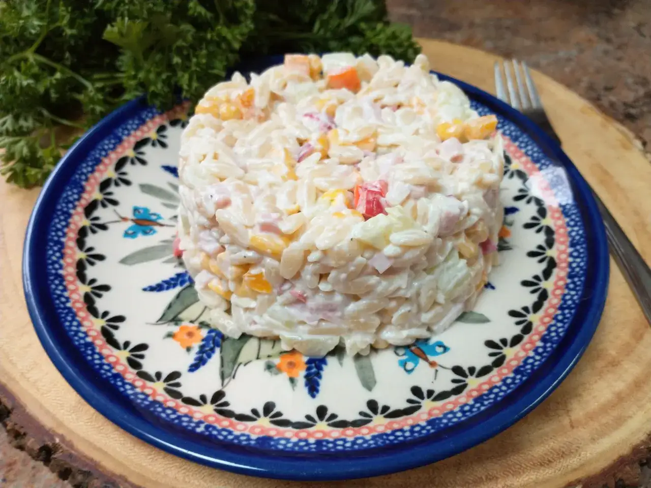 Pyszna sałatka z makaronem orzo, szynką i ogórkiem, podana na ozdobnym talerzu.