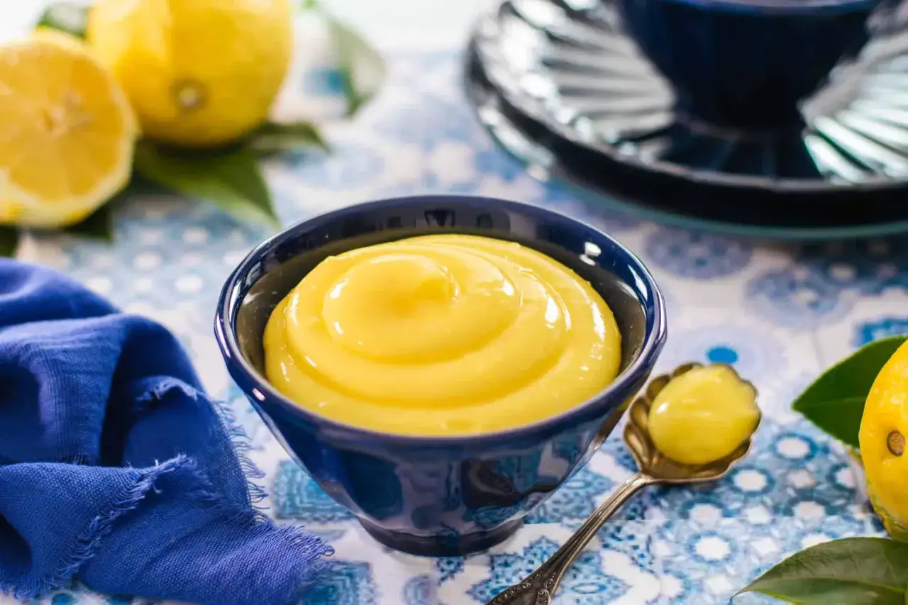 Crema di limoncello vellutata in una ciotola blu, con limoni freschi e un cucchiaino.