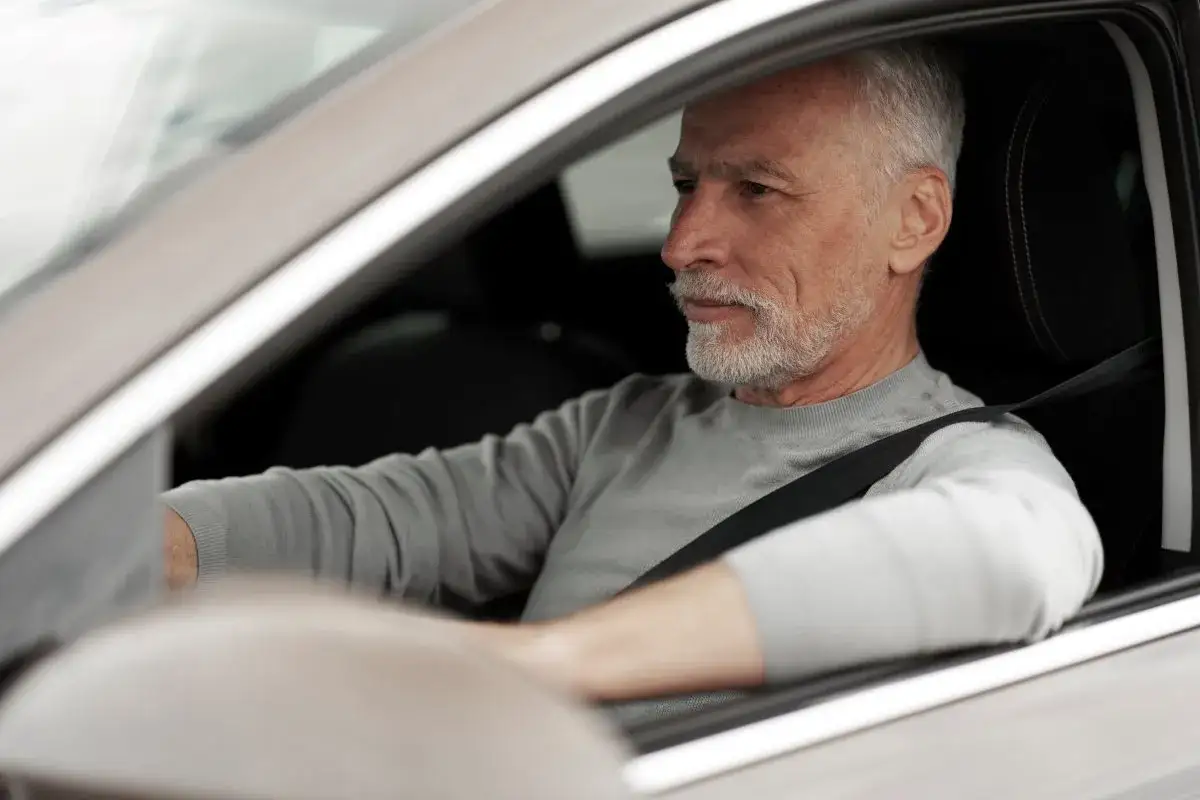 Hombre mayor con barba gris al volante, con cinturón de seguridad. Se pregunta hasta qué edad se puede conducir en España.