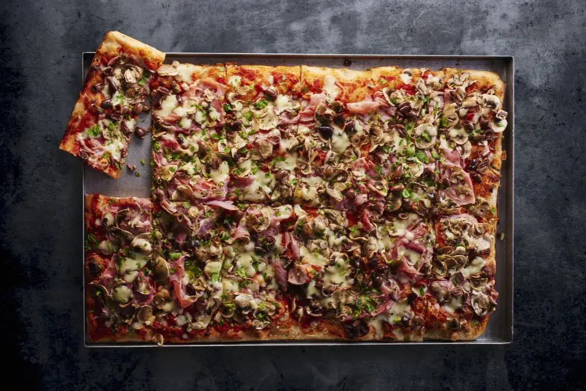 Domowa pizza na blachę z szynką, pieczarkami i oliwkami. Idealna na rodzinne spotkanie, przepis prosty i szybki.