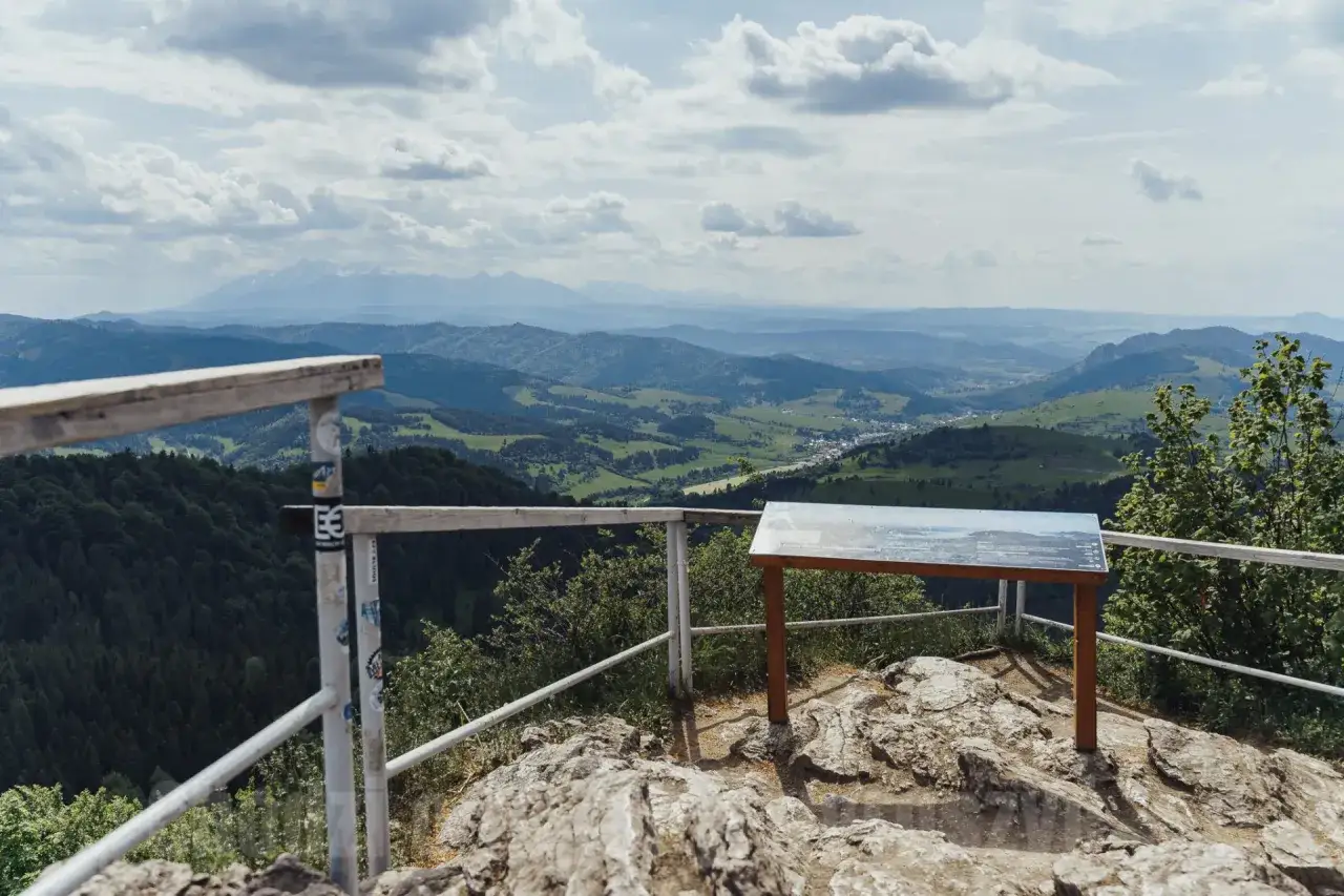Widok z **schroniska pod Durbaszką** na malowniczą dolinę i góry. Na pierwszym planie kamienie i barierka.