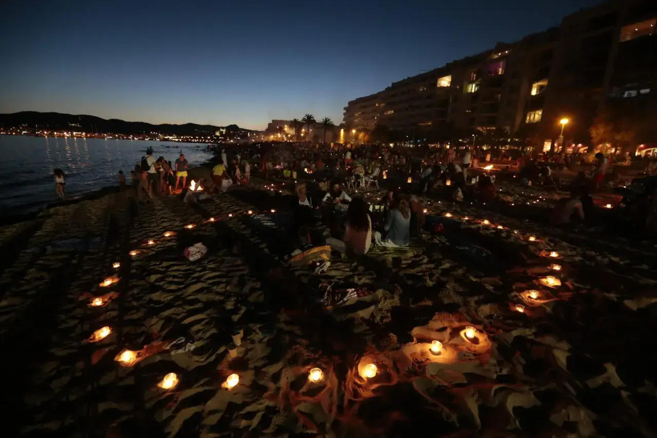 Una multitud en la playa al anochecer, con velas formando un camino para atraer el amor de una persona.