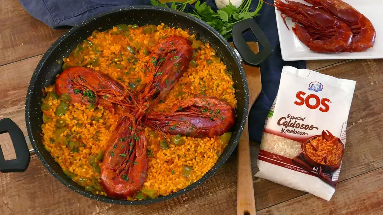 Arroz con carabineros, un plato vibrante con gambas rojas y arroz amarillo en una paellera, junto a un paquete de arroz SOS.
