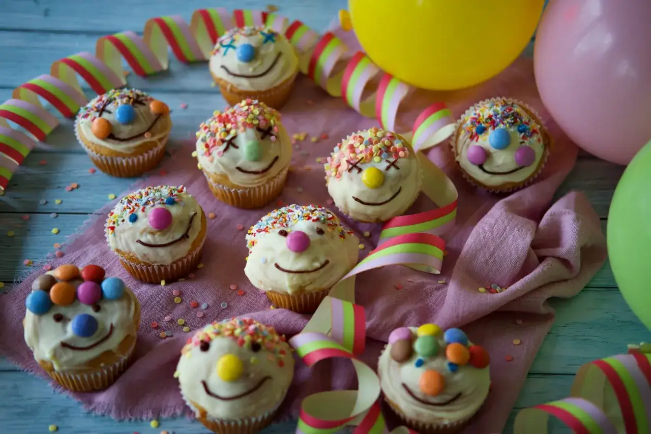 Bunte Fanta Muffins mit lustigen Gesichtern und Konfetti, dekoriert mit Luftballons und Partygirlanden.