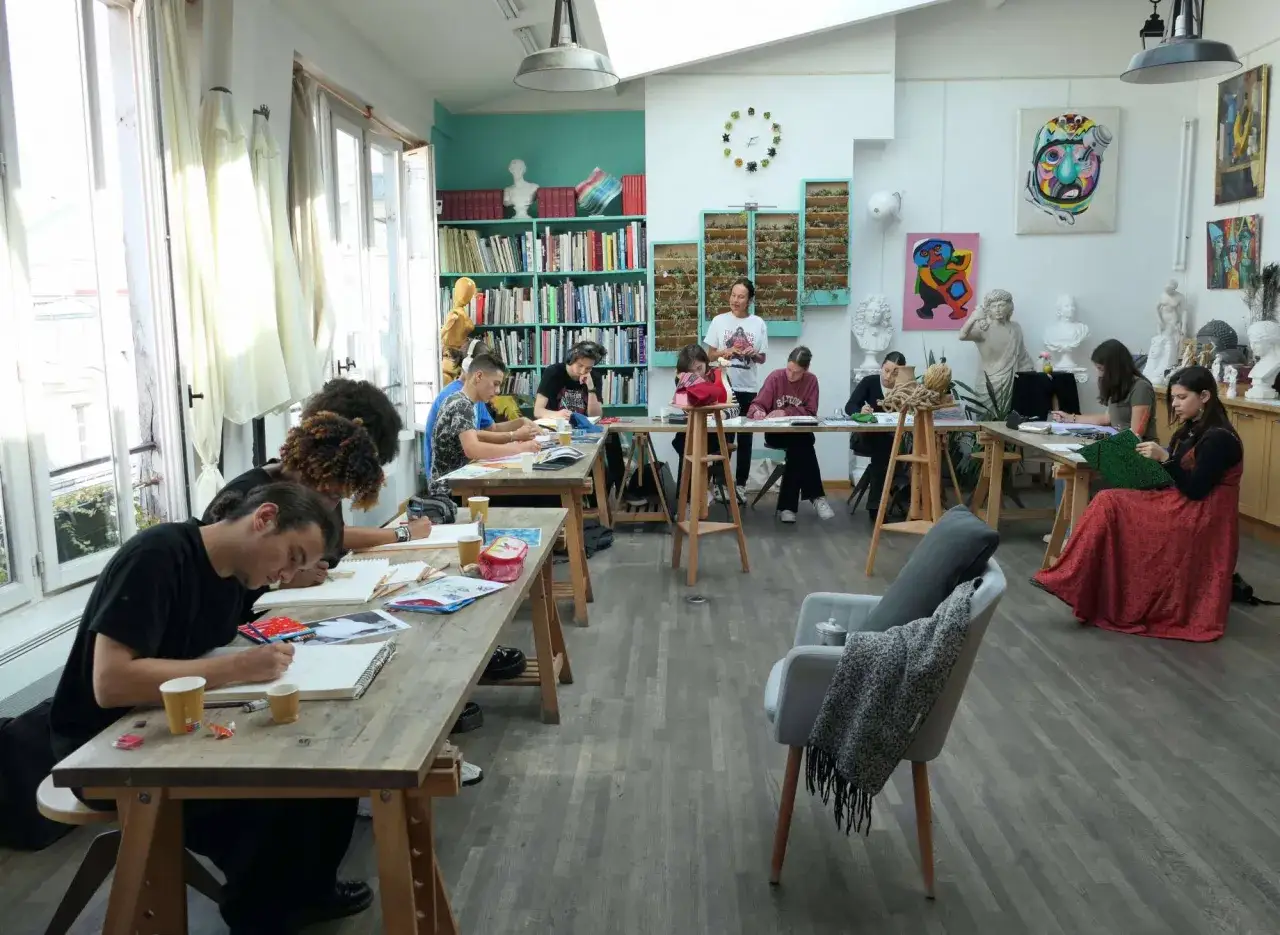 Dans une &eacute;cole d'arts, des &eacute;tudiants dessinent &agrave; des tables en bois, sous le regard d'un professeur.