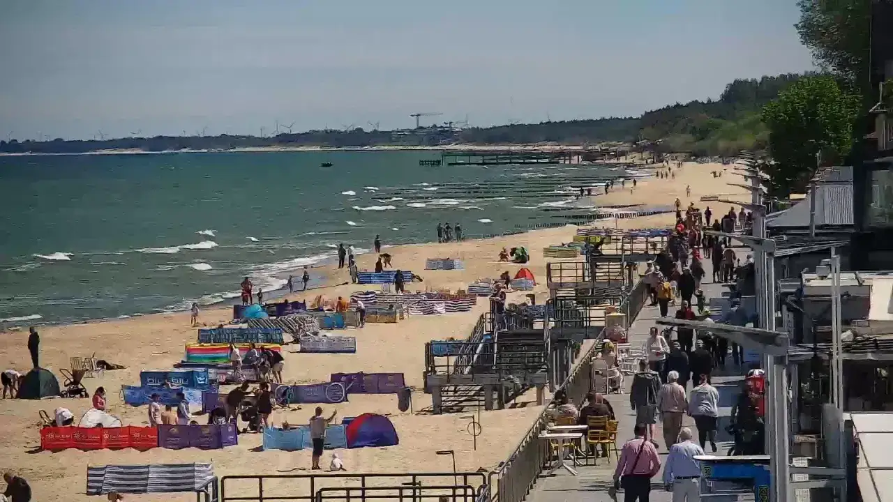 Słoneczna plaża w Sarbinowie tętni życiem. Ludzie spacerują, odpoczywają pod parawanami, a fale Bałtyku zachęcają do kąpieli. To idealne miejsce na wakacyjne atrakcje.