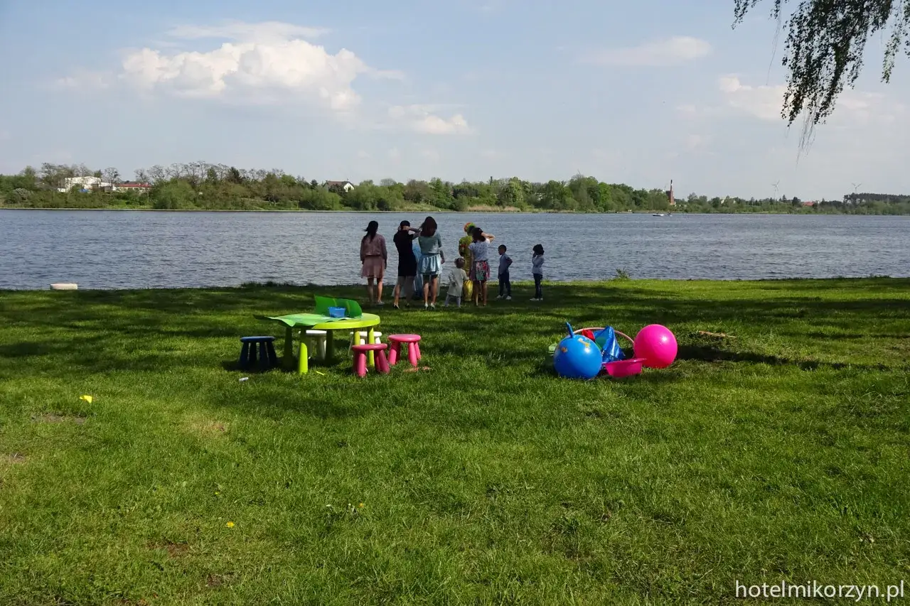Rodzina odpoczywa nad jeziorem Mikorzyńskim. Na trawie kolorowe zabawki i stolik dla dzieci.