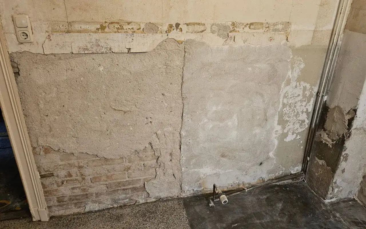 Abblätternder Putz enthüllt Ziegelmauerwerk. Die Wand zeigt Risse und Verfärbungen, die auf mögliche Probleme hinweisen, die man bei der Suche nach asbest erkennen sollte.
