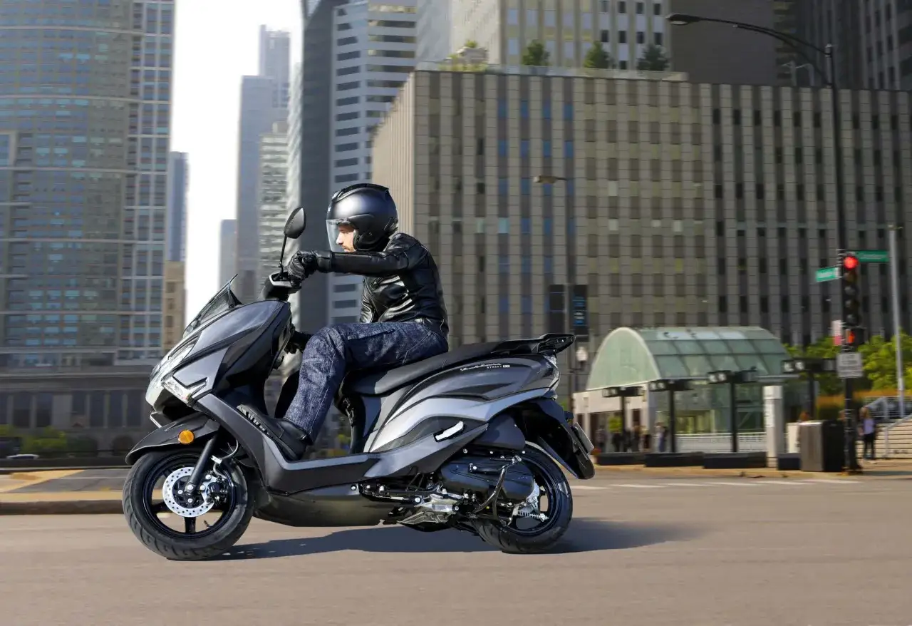 Mężczyzna w kasku i skórzanej kurtce jedzie skuterem Suzuki Burgman 125 po mieście. Sprawdź suzuki burgman 125 cena!