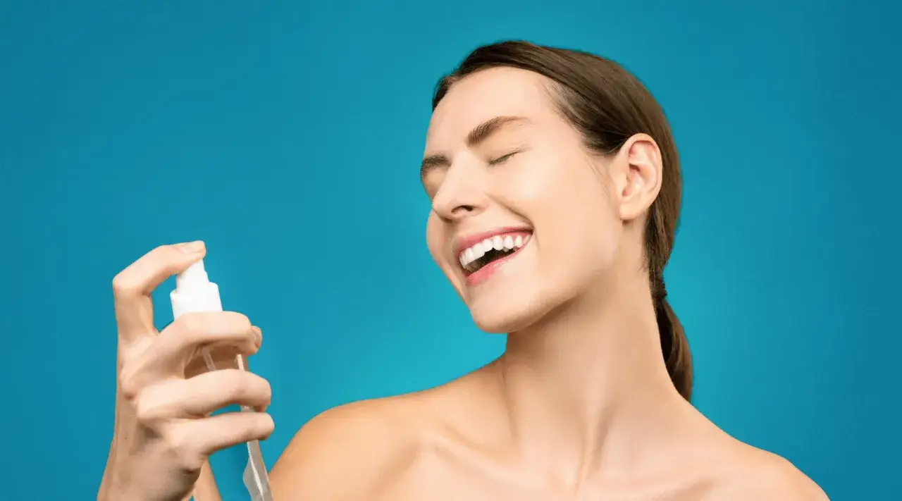Une femme rit sous un spray de lotion tonique visage. Ce produit sert à rafraîchir et hydrater la peau.