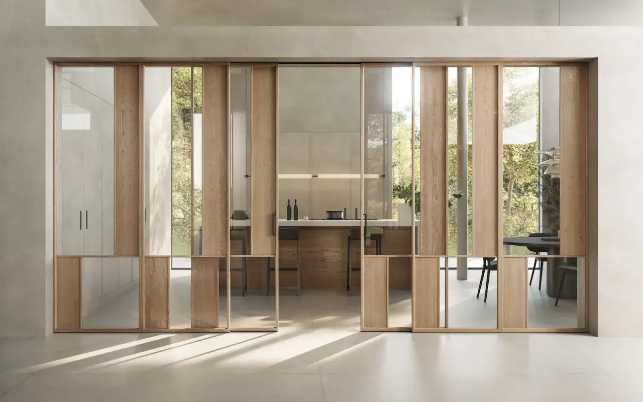Porta scorrevole in legno e vetro, con un design che evoca lo **stile brutalista** nella sua essenzialit&agrave; materica, apre su una cucina moderna.
