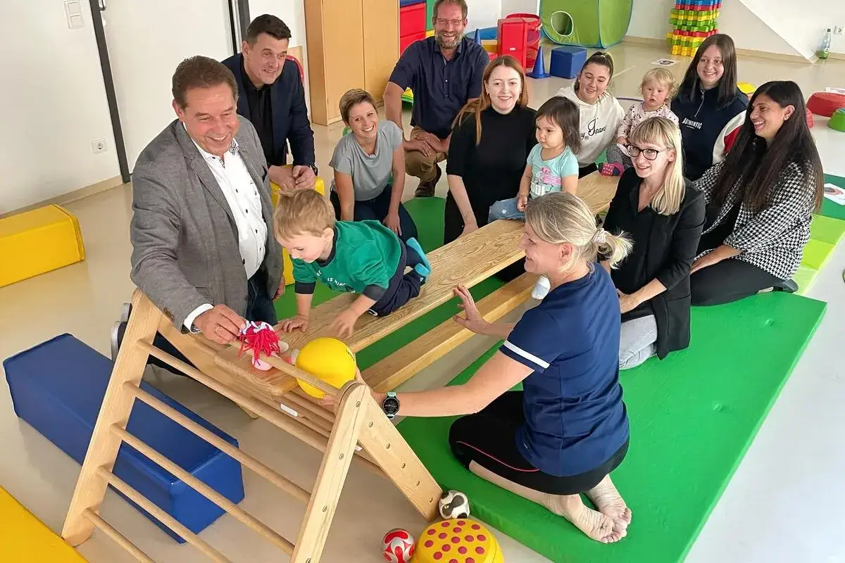 Erwachsene beobachten ein Kind, das auf einem Holzspielger&auml;t klettert. Der **Bewegungsdrang** von **Kindern** wird hier gef&ouml;rdert.