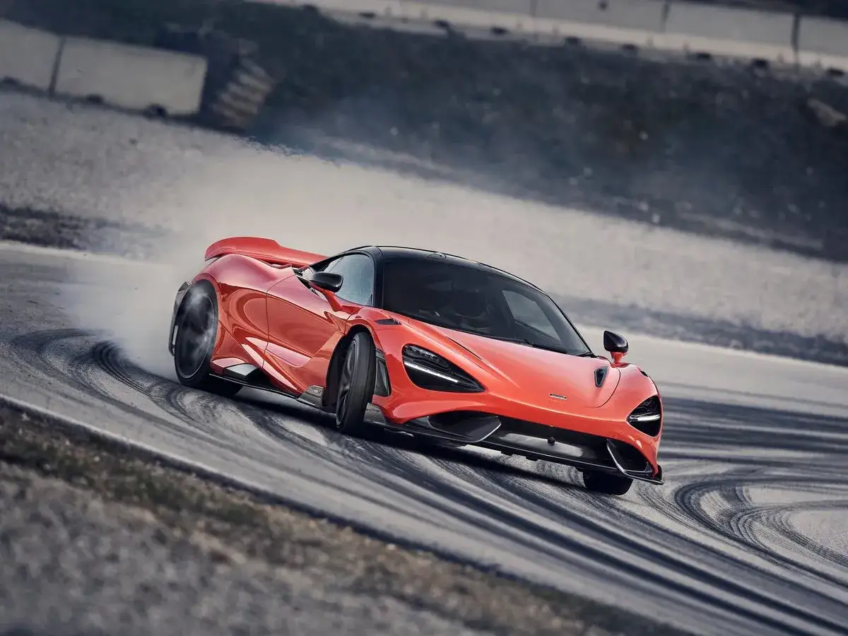 Pomarańczowy McLaren 765LT z gracją driftuje po torze, zostawiając za sobą kłęby dymu.