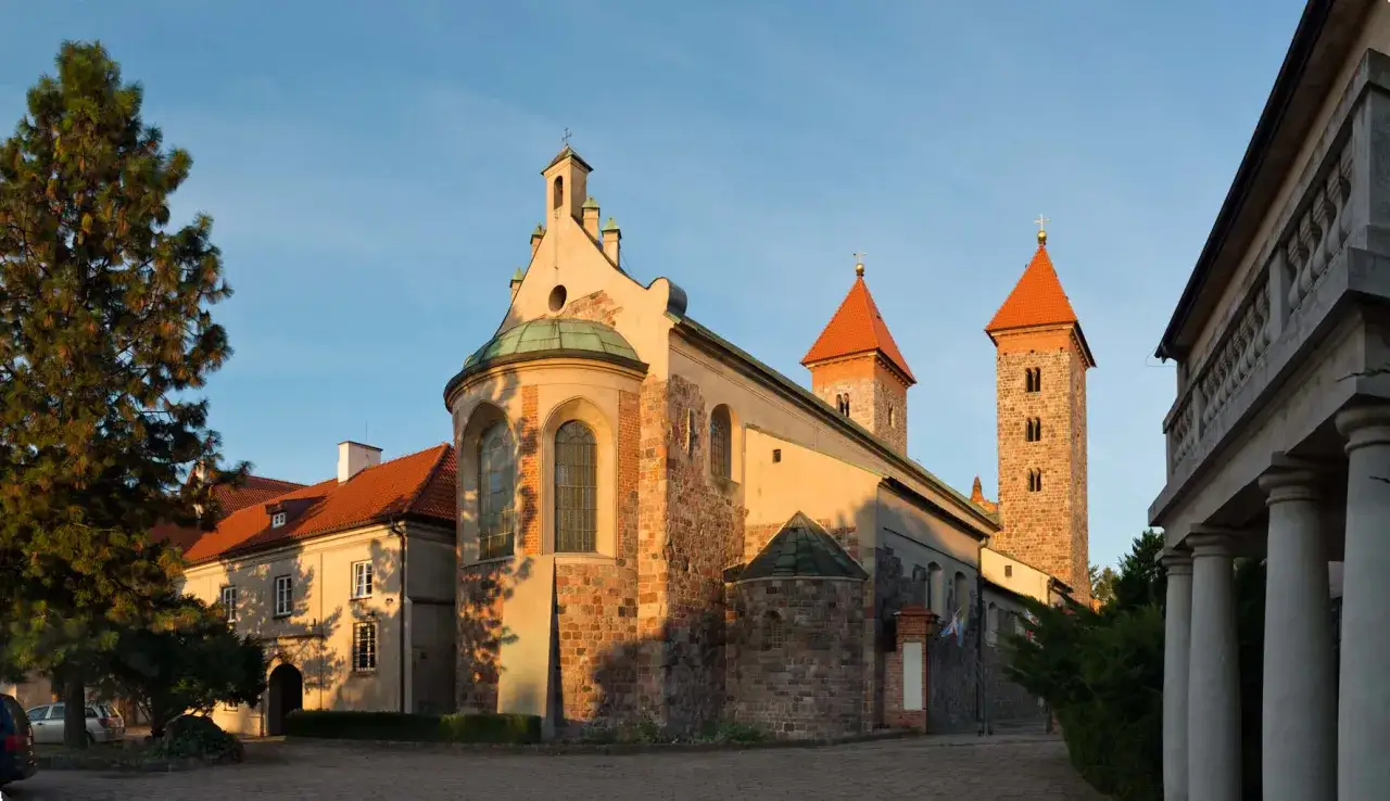 Zabytkowa bazylika w Czerwińsku nad Wisłą o zachodzie słońca. Kamienne mury i czerwone dachy wież tworzą malowniczy widok.