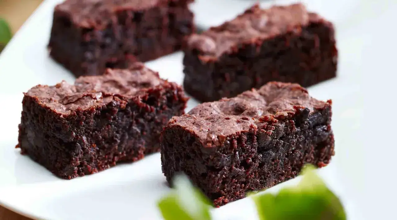 Vier saftige fudge brownie St&uuml;cke auf einem wei&szlig;en Teller, bereit zum Genuss.