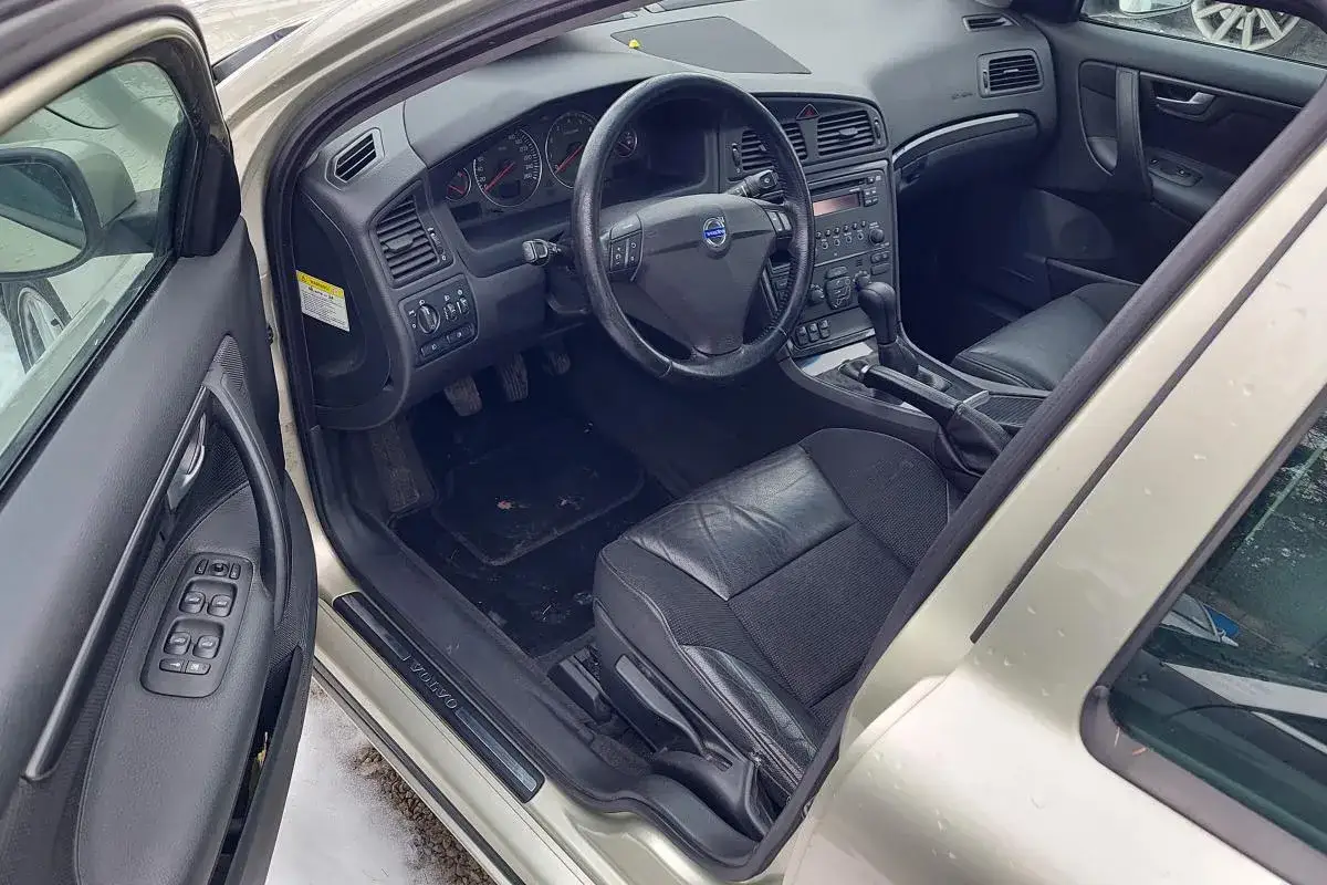 Wnętrze Volvo S60 2005 z czarną skórzaną tapicerką, kierownicą i deską rozdzielczą.