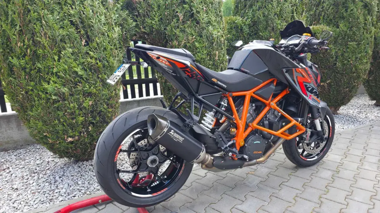 Czarny KTM 1290 Super Duke z pomarańczową ramą i wydechem Akrapovič, gotowy do jazdy.