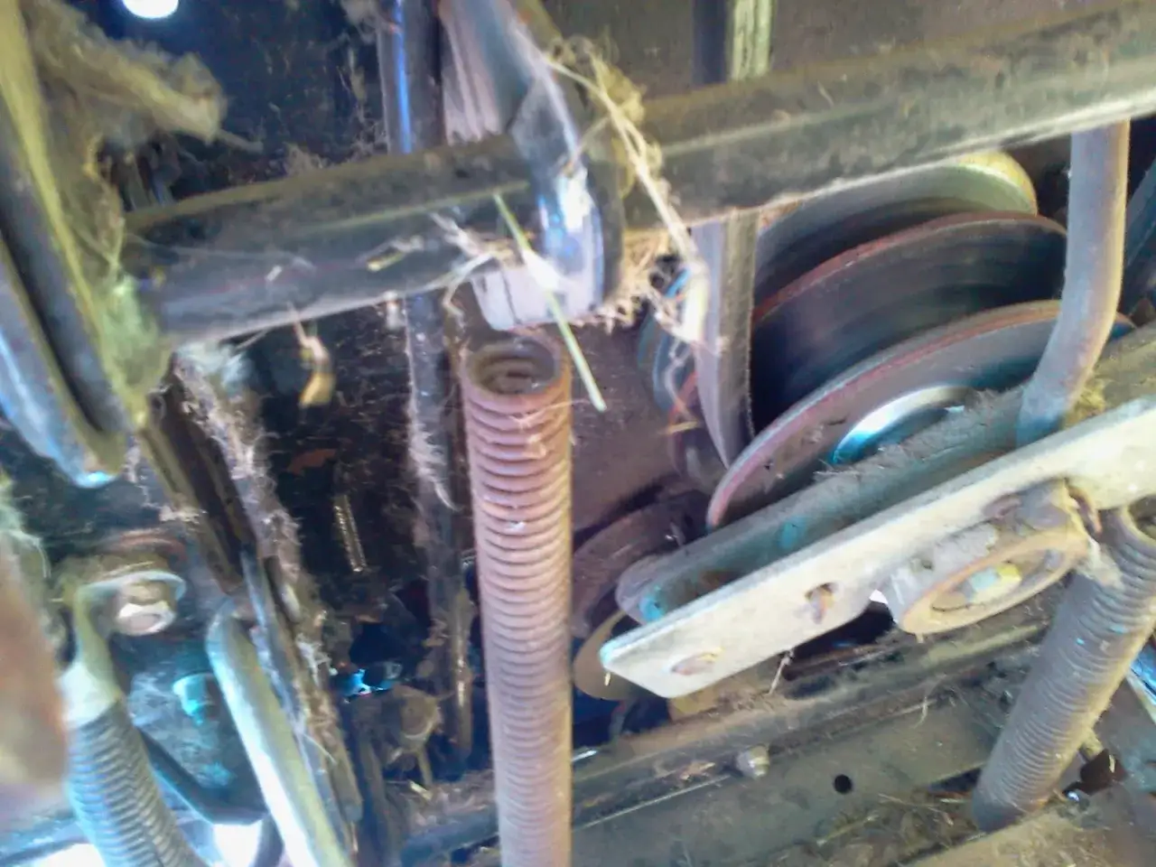 Mechanizm napędowy kosiarki traktorka MTD, z widocznym pasem, sprężyną i kołami pasowymi. Pasek do kosiarki traktorka MTD wymaga precyzyjnego montażu.