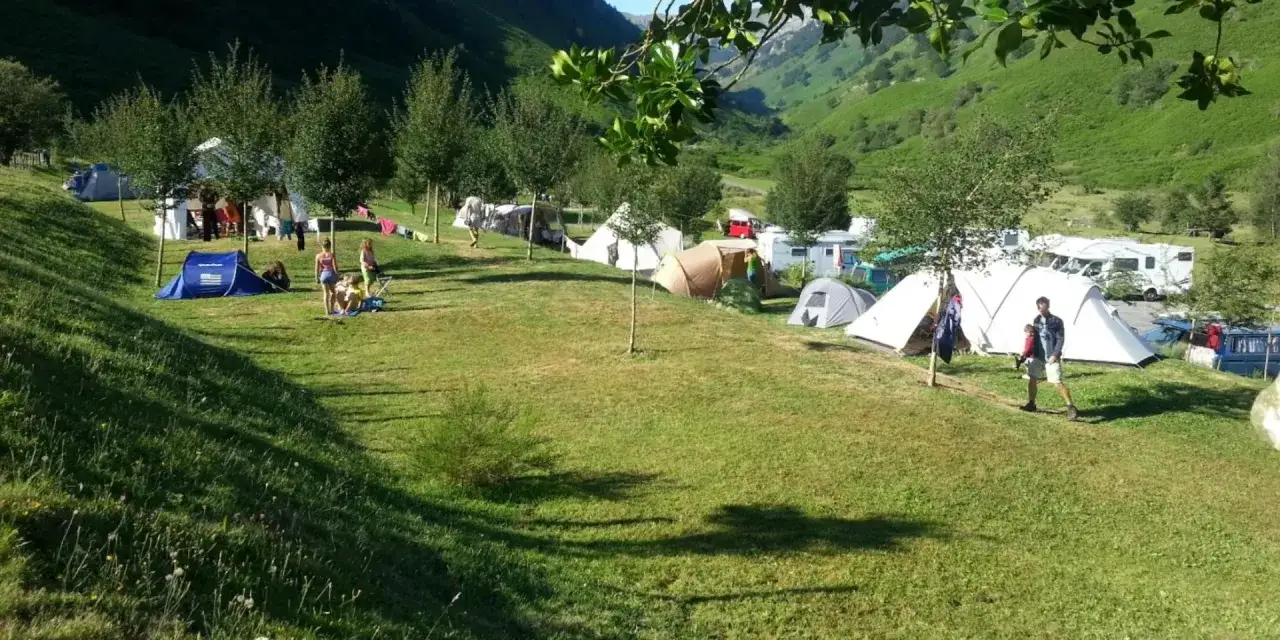 Acampada familiar en el Pirineo francés. Tiendas de campaña y caravanas en un valle verde, con niños jugando y disfrutando del aire libre.