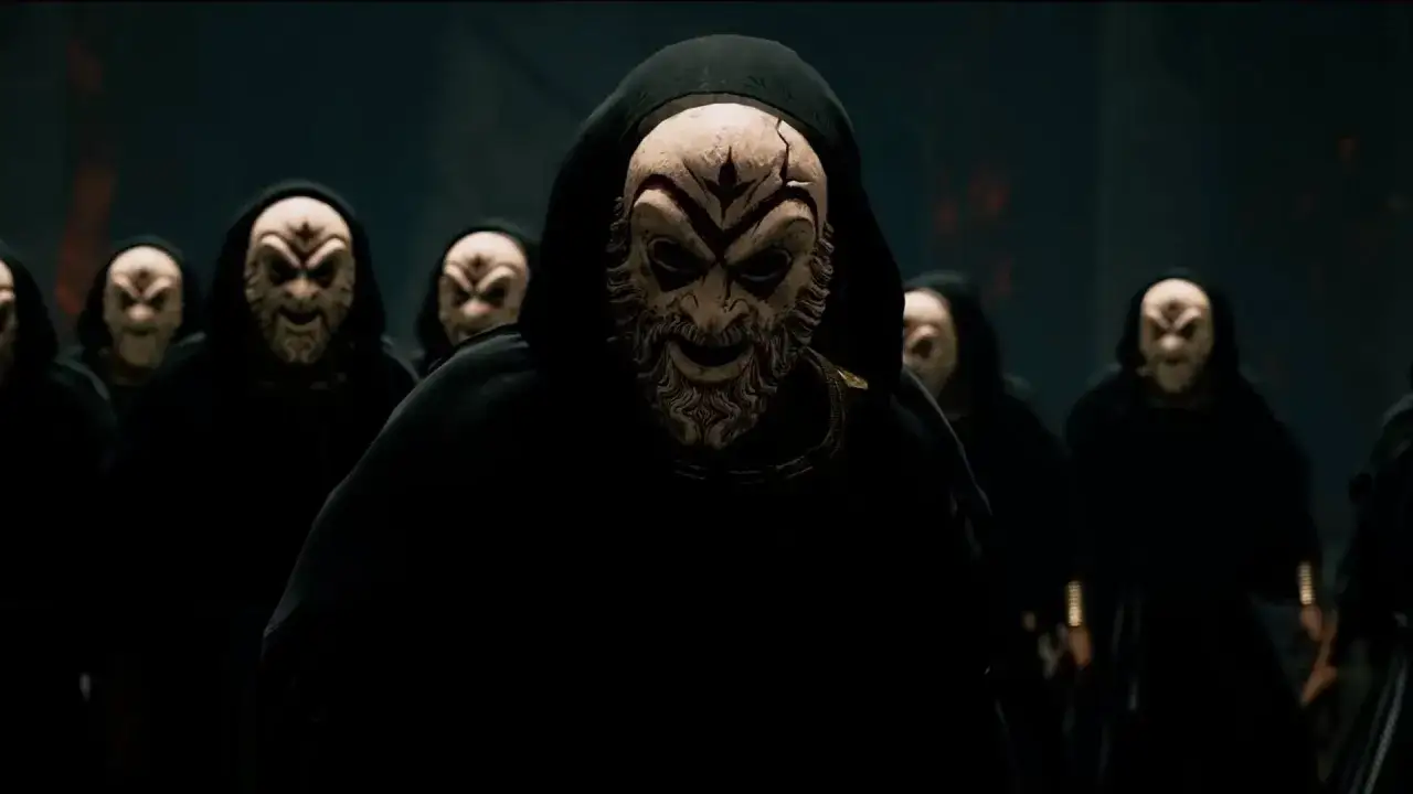Miembros del culto de Kosmos, con t&uacute;nicas negras y m&aacute;scaras grotescas, se re&uacute;nen en la penumbra.