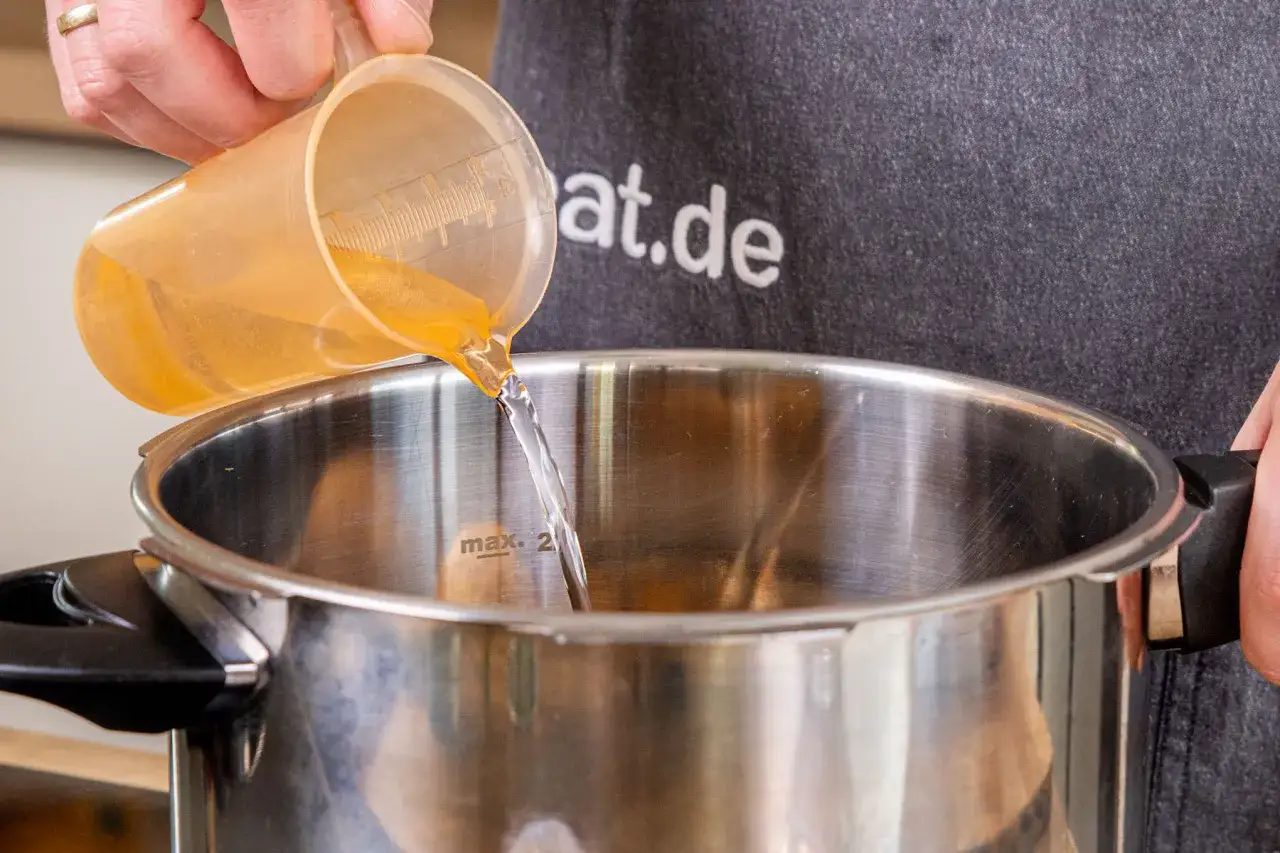 Fl&uuml;ssigkeit wird in einen Schnellkochtopf gegossen, bereit f&uuml;r die Zubereitung von Kartoffeln.
