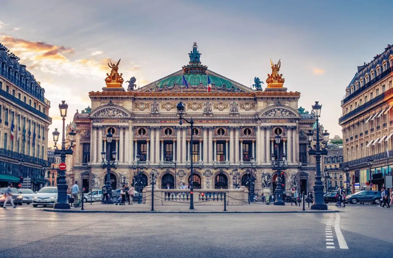 Słynny teatr w Paryżu, Opera Garnier, z bogatą fasadą i złotymi rzeźbami, oświetlony zachodzącym słońcem.