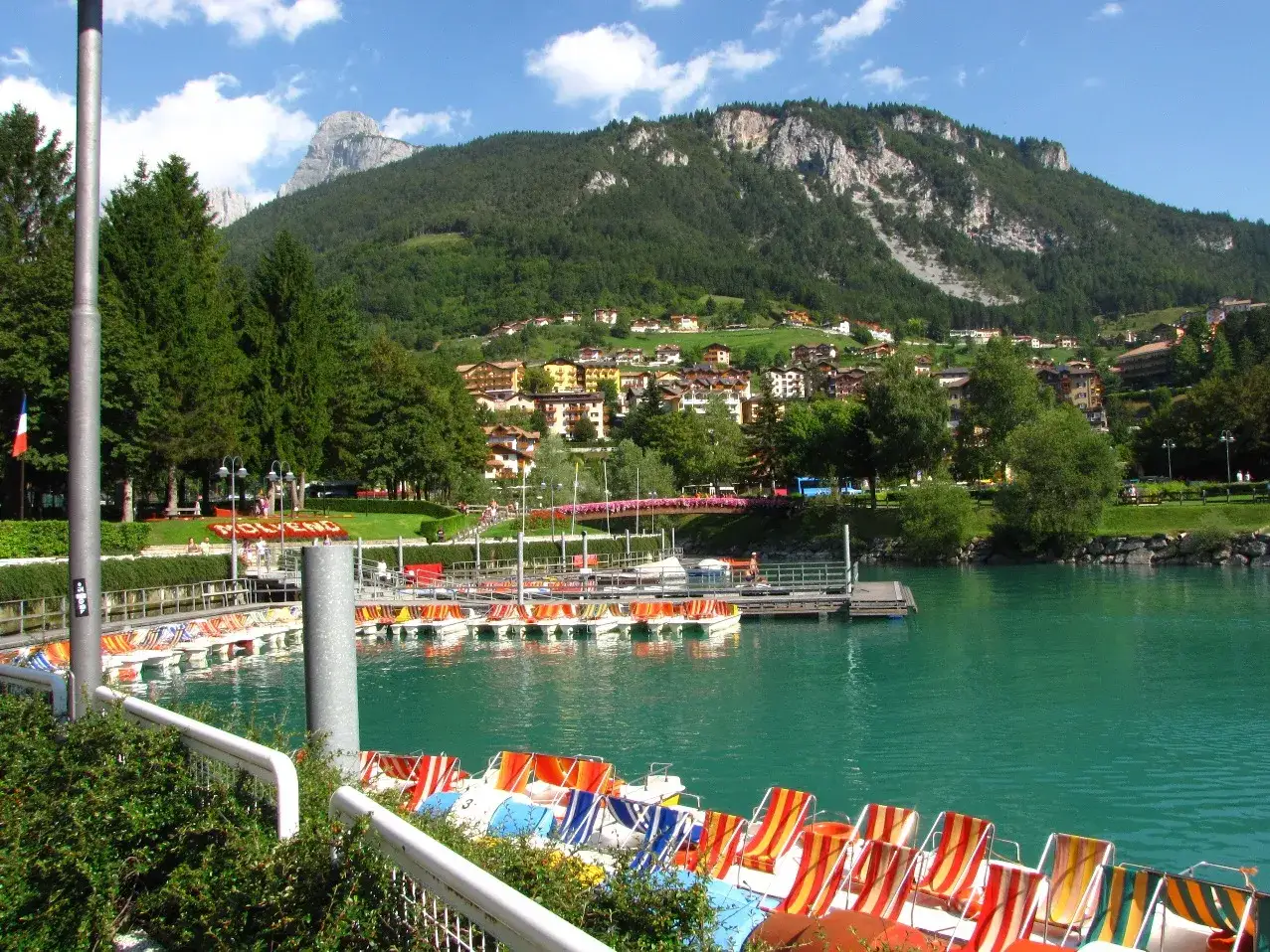 Pedalò colorati attendono sul lago di Molveno, con il paese e le montagne sullo sfondo.