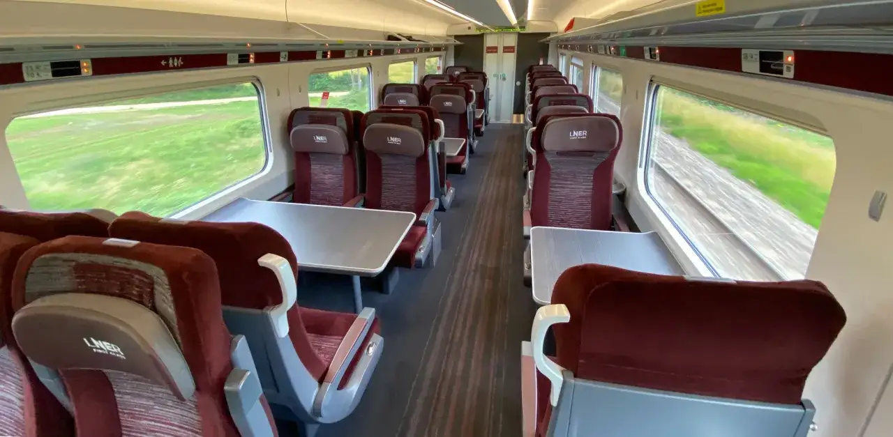 Tomma säten i ett tåg, troligen på väg till London. Fönstren visar gröna fält som svischar förbi.