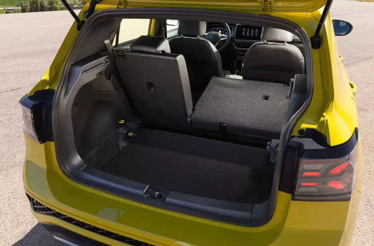 Żółty Volkswagen T-Cross z otwartym bagażnikiem, pokazujący przestronne wnętrze i złożone tylne siedzenia, gotowe na każde wyzwanie.