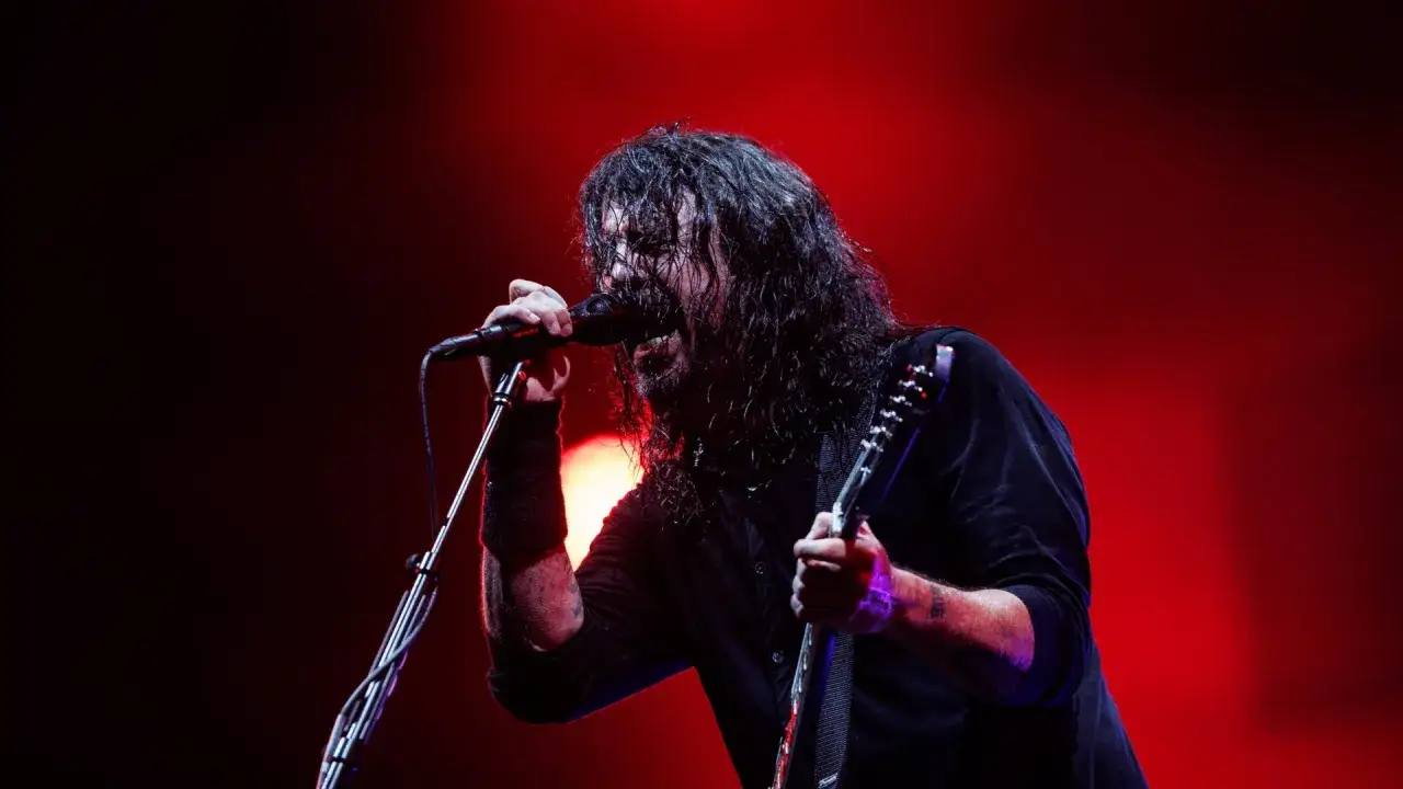 Dave Grohl z zespołem na scenie, śpiewający do mikrofonu i grający na gitarze.